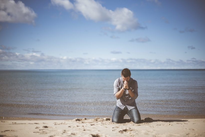 Hình ảnh cầu nguyện chàng trai ngồi giữa bãi biển