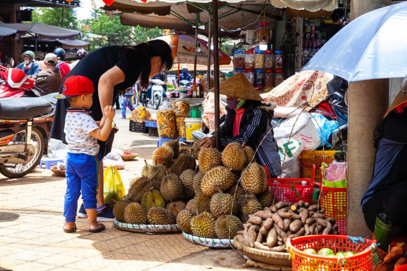 A Vietnamese woman with a boy buys durian on the street of Da La